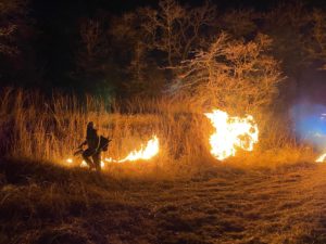 Fireman walks along a fire line with fire resources in the dark of night with only the glow of the fire