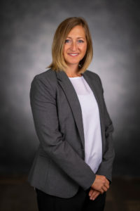 A woman, Stacy Hines, stands in a gray jacket