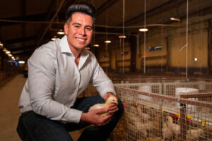 Daniel De Leon kneeling in a barn holding a baby chick