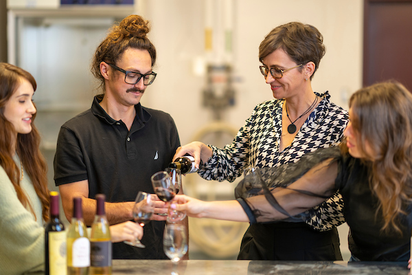 Dr. Andreea Botezatu, enology specialist, pours glasses of wine for her students to taste.