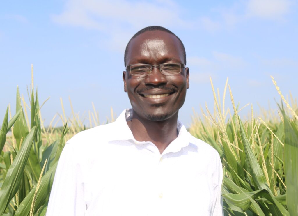Head and shoulder photo of Peter Omara, Ph.D., in white shirt standng in a field.