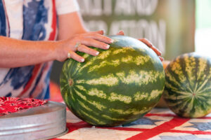 A woman with two watermelons on a table.