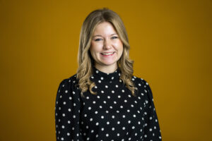 Head and shoulders of Presley Wirebaugh wearing a black long sleeve shirt with a yellow background.