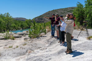Five individuals use cameras and binoculars in an outdoor setting.