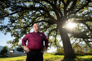 Mike Arnold stands under a tree with the sun shining through the branches