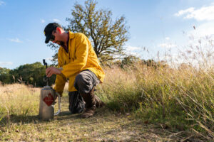 A man in a yellow jacket prepares a drip torch for a prescribed fire.