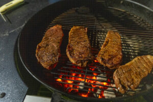 Three steaks cook on a grill.