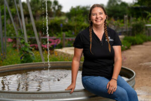 A woman in a black polo and jeans sits on the edge of a small pool.