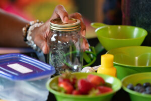 A hand holding a jar for food preservation, with bowls of fruit around it