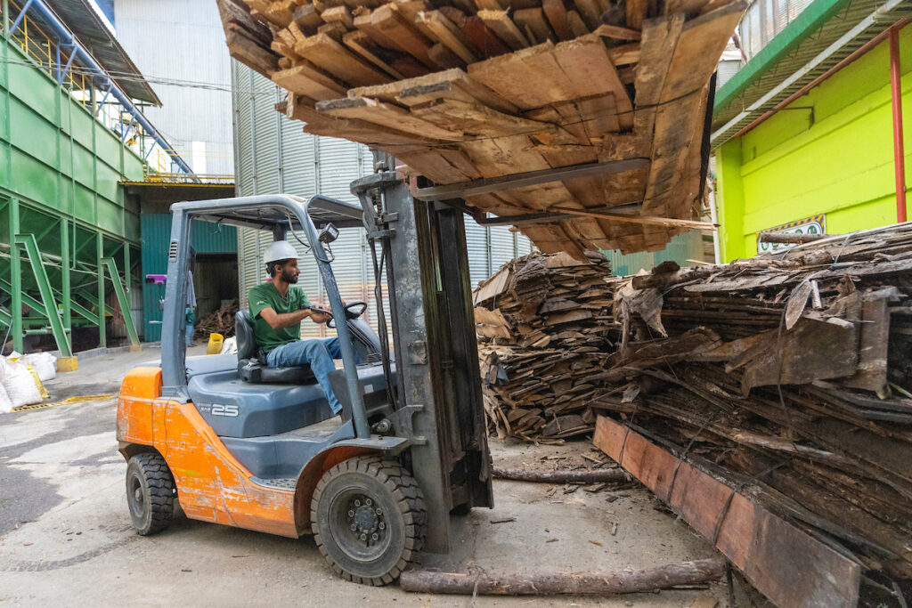 An orange forklift moves wood. 