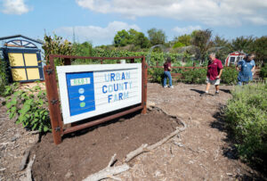 A sign that says Urban County Farm with people walking around.