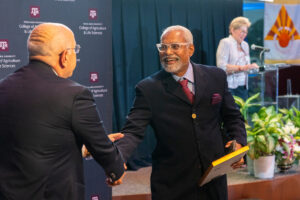 A man in a suit and glases shakes the hand of another man in a suit at a banquet style event indoors.