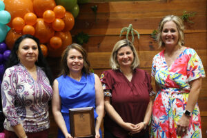 four women standing, one with a plaque in her hands