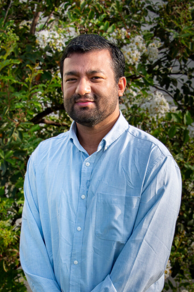 Pramir Maharjan in blue shirt stands in front of tree