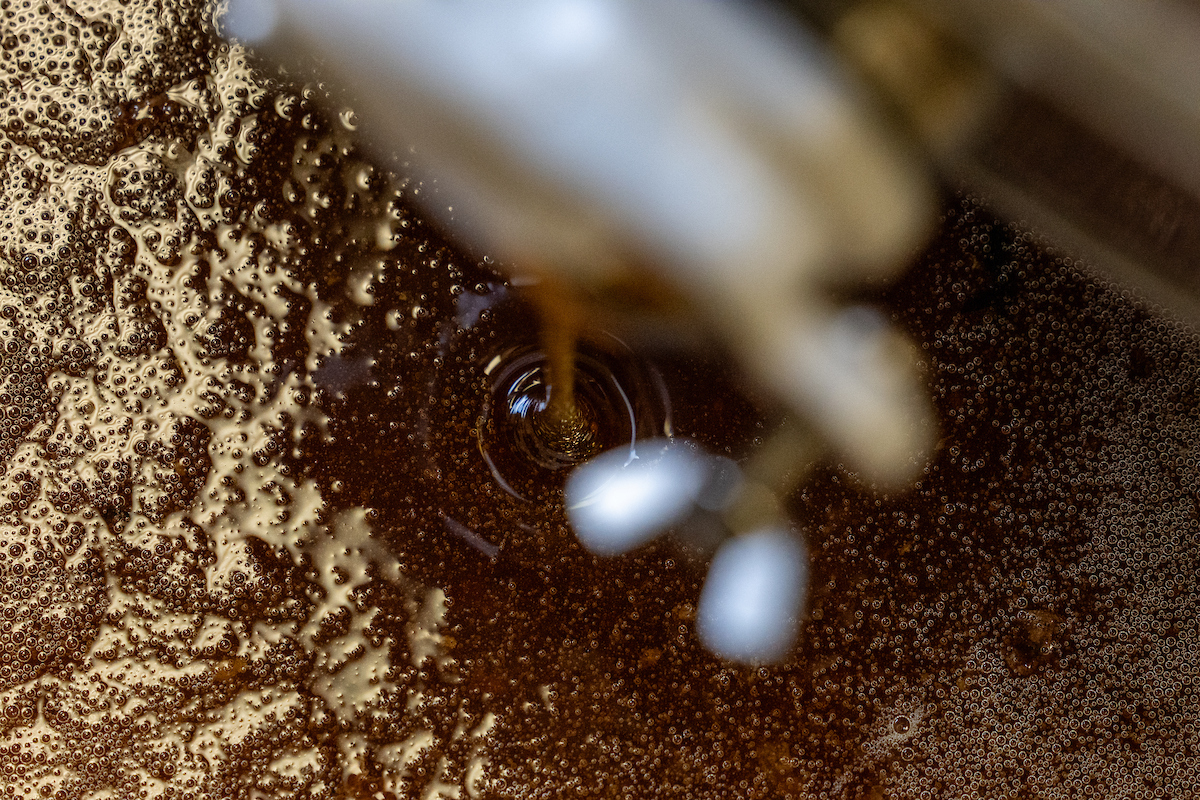 Honey dripping into a large stainless steel container.
