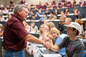 Man shakes hands with a seated student in a large classroom.