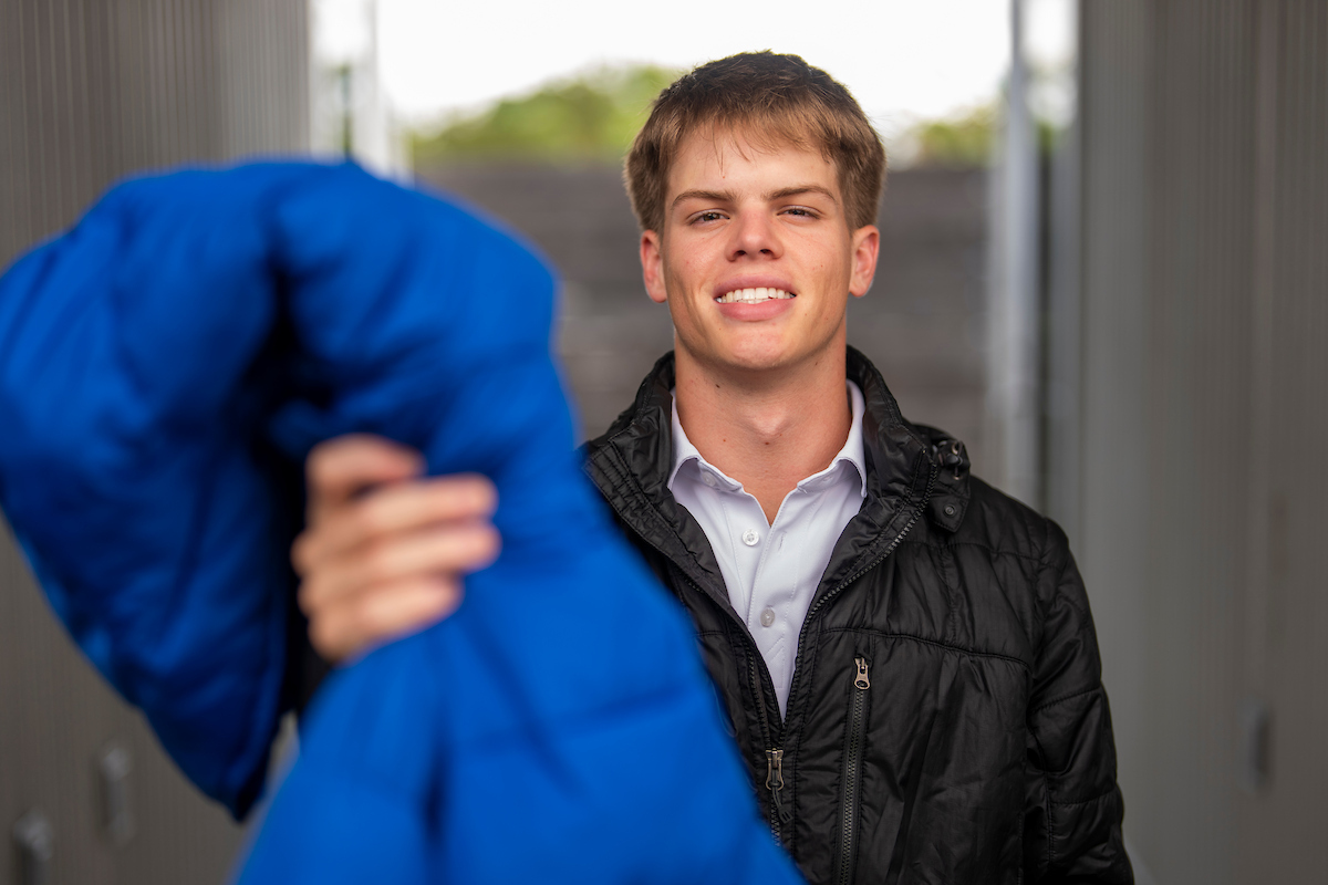 A man in a black coat reaches out with a blue coat in hand.