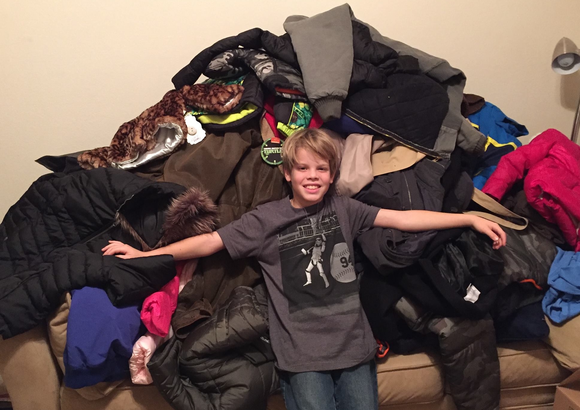 A child sitting with a large pile of coats.