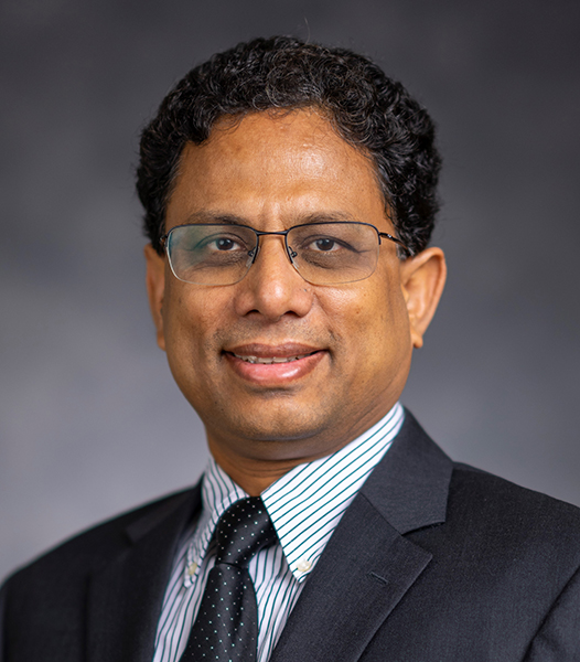 Binyak Mohanty stands in front of gray background wearing a suit and tie.