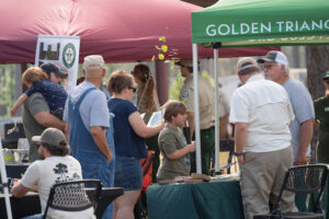 people are gathered around an exhibitor both with a green awning.