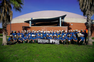 a large group of students posing behind a sign that says Sisters in Fire