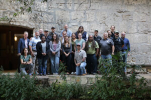 a group of 22 people standing next to a stone wall