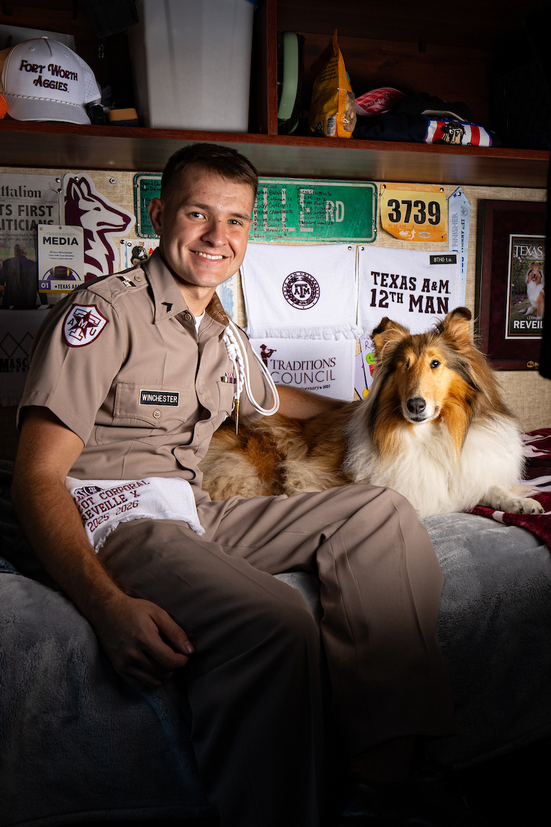 Man in light brown uniform poses with dog and smiles.