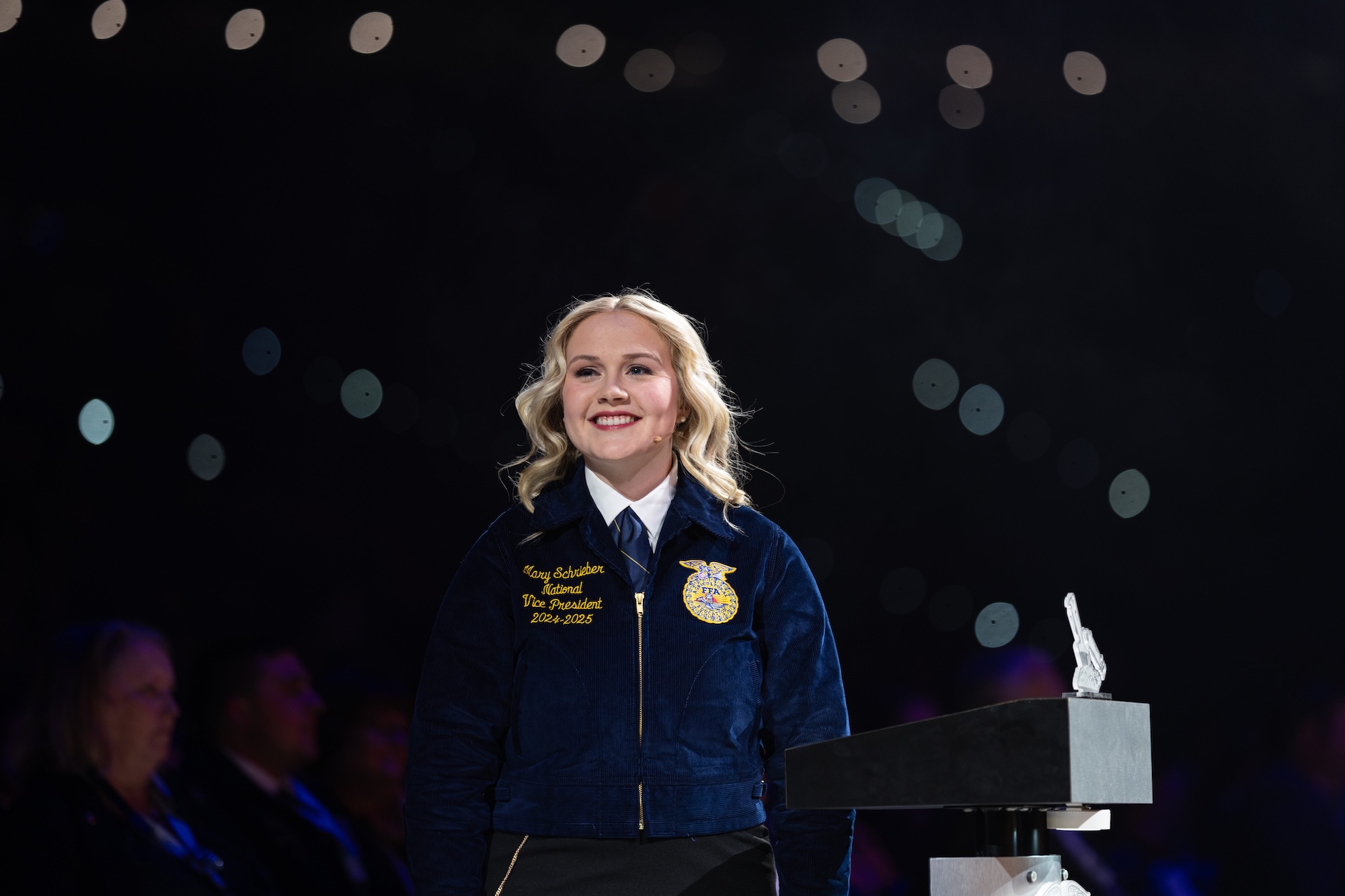 A woman in a blue jacket smiles on a stage.